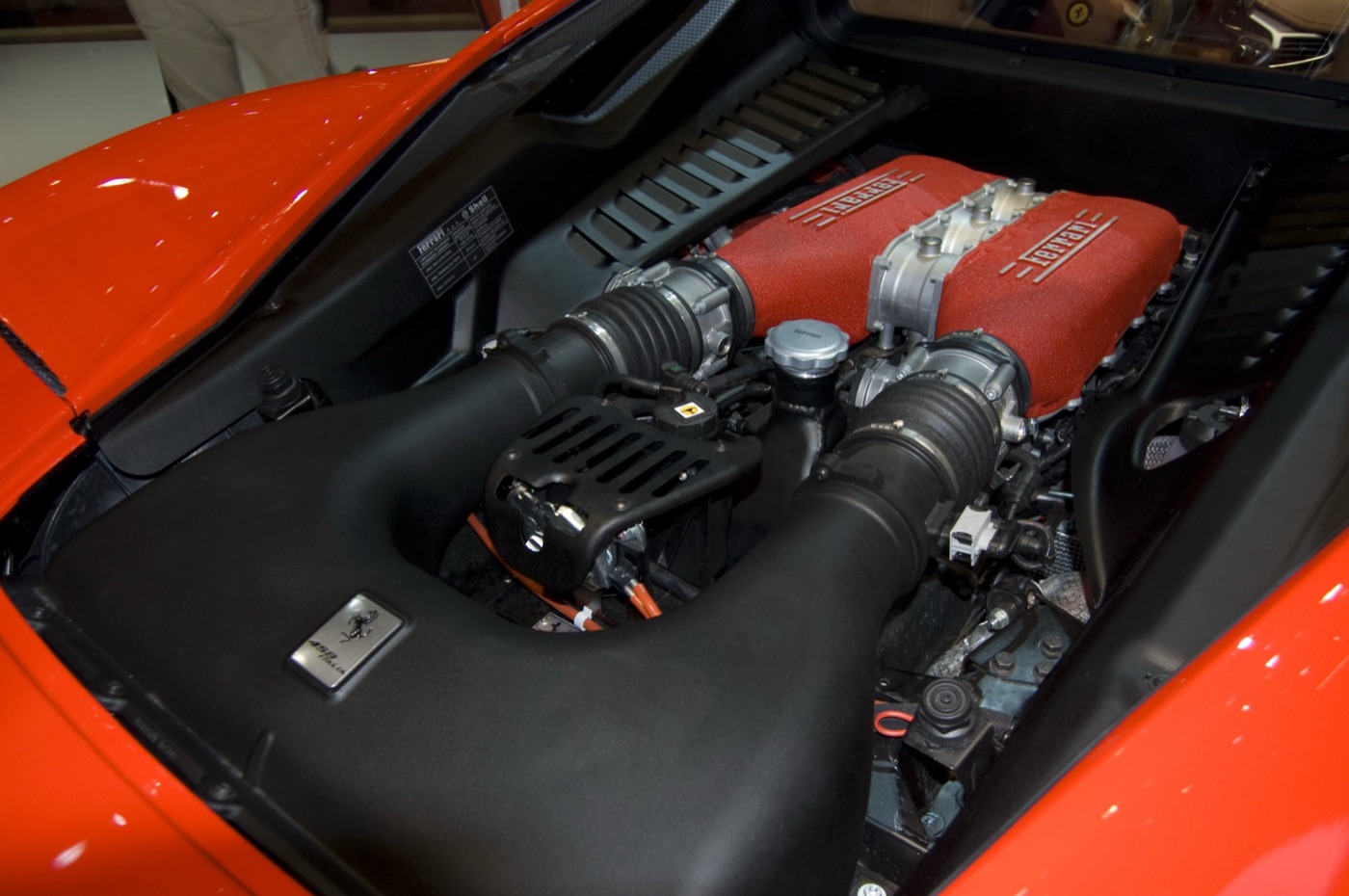 The 4.5-litre V8 engine of a Ferrari 458 Italia with red intake plenums stamped Ferrari, seen through the open engine bay