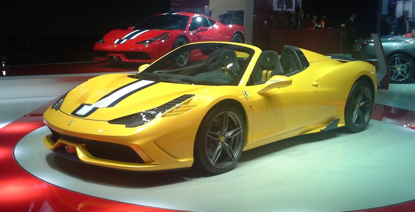 Yellow Ferrari 458 Speciale A with white and black stripes on a turntable at the Paris motor show, a red Speciale behind