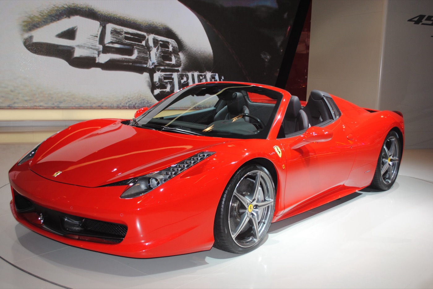 Red Ferrari 458 Spider with its roof down on a motor show turntable in front of a 458 Spider sign