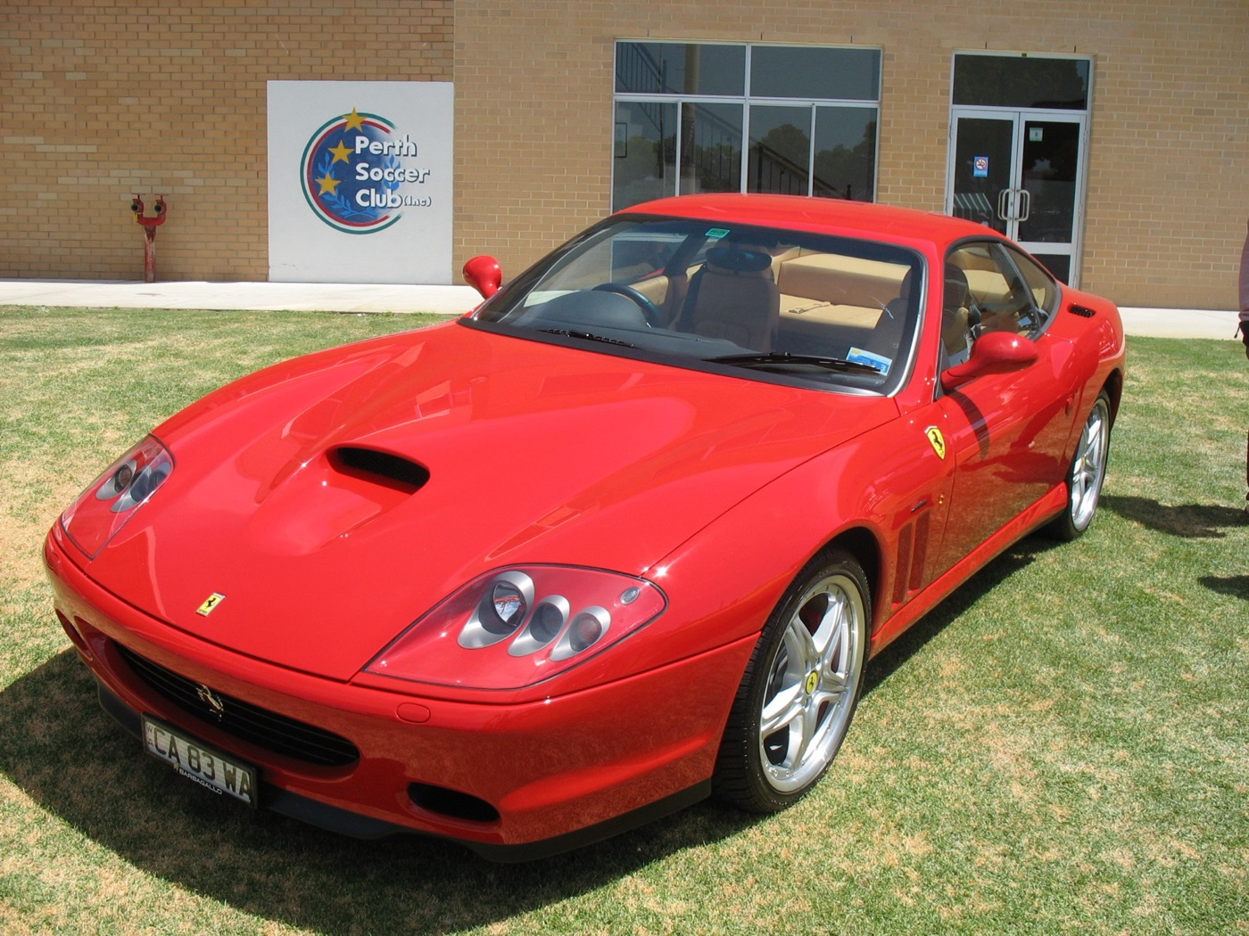 Red Ferrari 575M Maranello coupé with a bonnet scoop, parked on grass