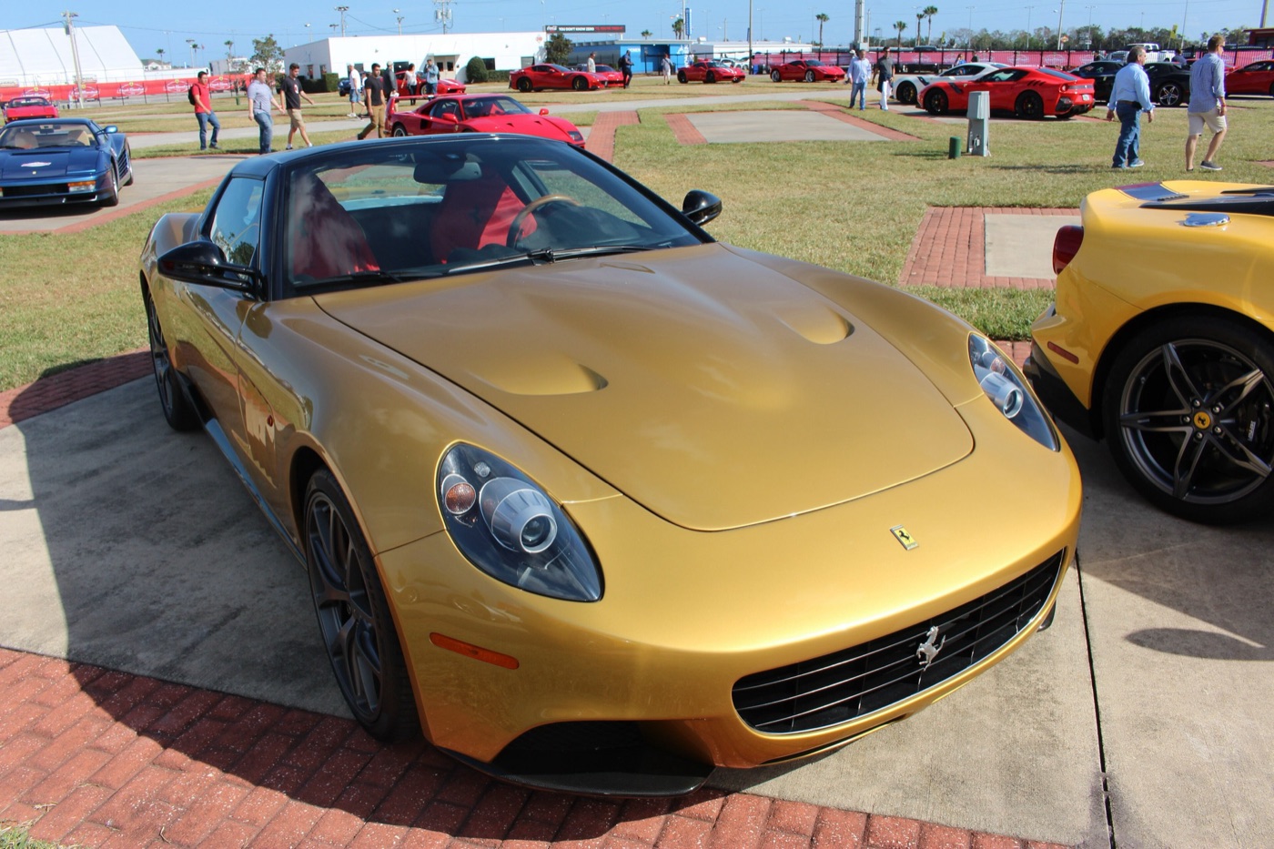 Gold Ferrari P540 Superfast Aperta with a black roof, parked on a path between lawns
