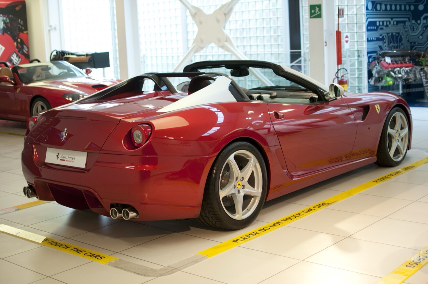 Dark red Ferrari 599 SA Aperta roadster seen from the rear left, with fins behind the seats, in a museum