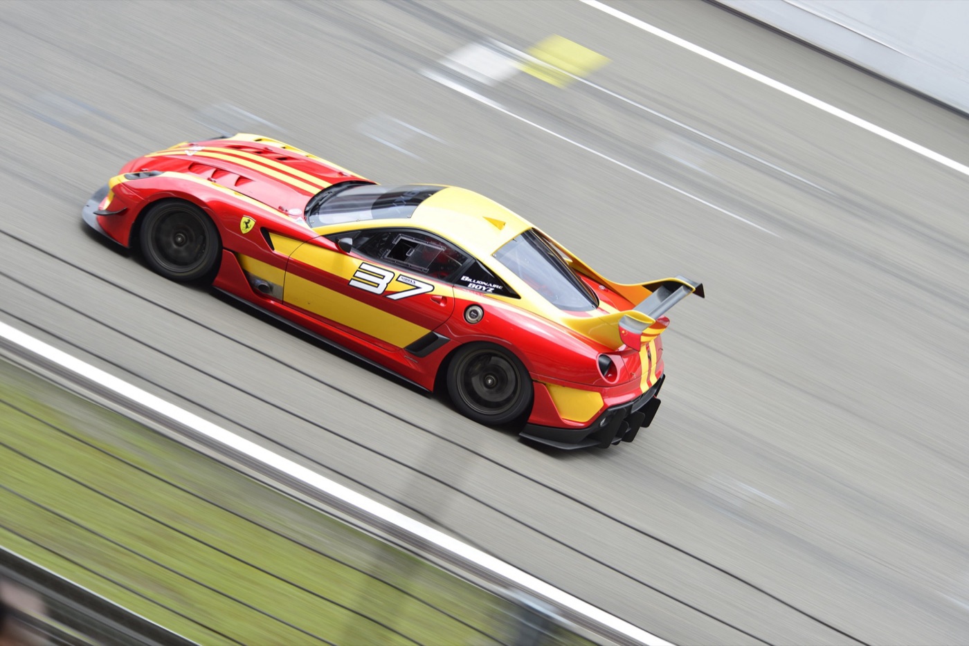 Red and yellow Ferrari 599XX with race number 37 at speed on a circuit, with its rear wing raised