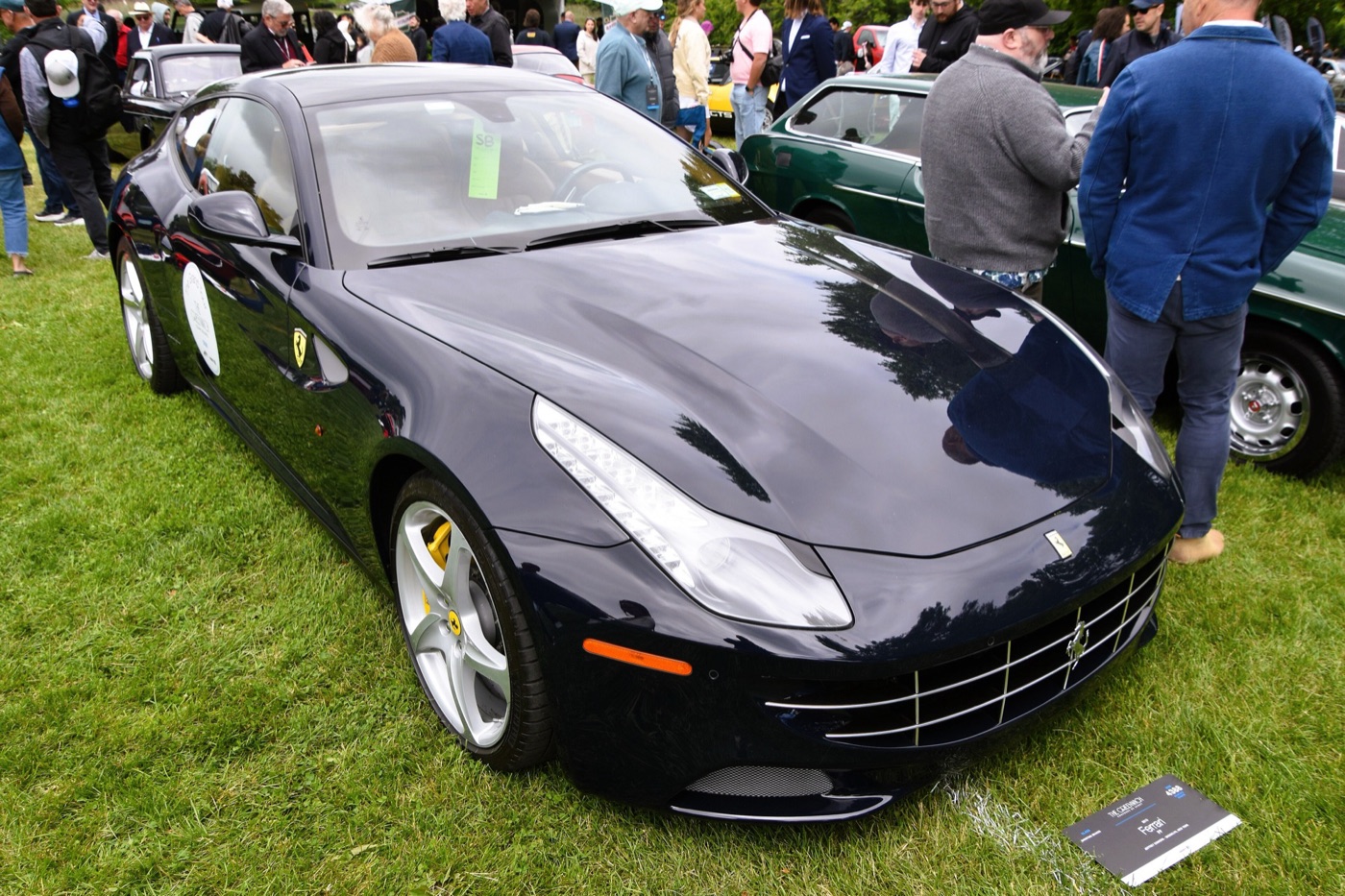Black 2013 Ferrari FF parked on grass at a concours, with an information card in front of it