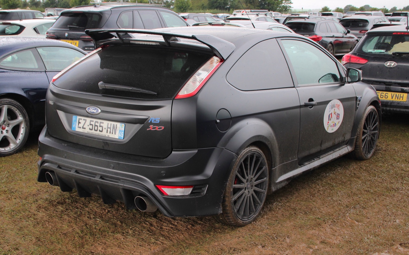 Mud-spattered matt black Focus RS500 with French plates in a grass car park, seen from the rear