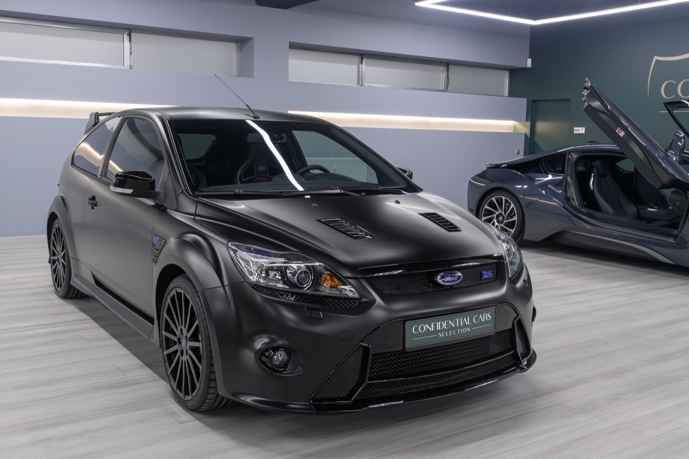 Matt black Ford Focus RS500 for sale in a dealer showroom beside a BMW i8