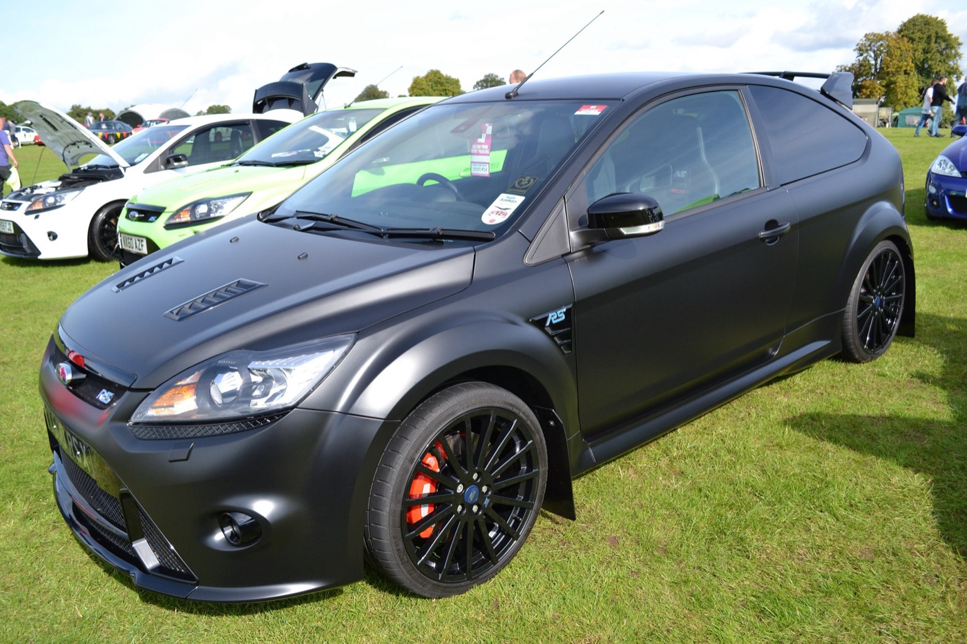 Matt black Ford Focus RS500 with black wheels and red brake calipers parked on grass at a car show