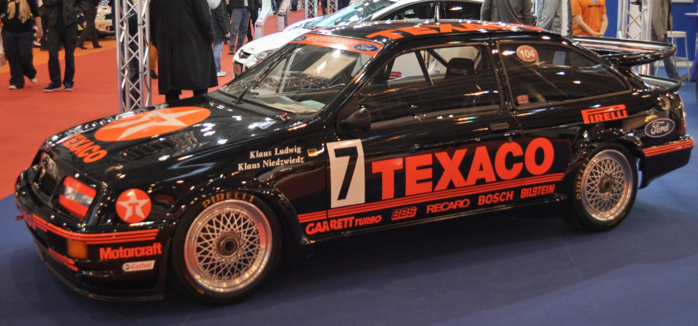 Black Texaco-liveried Ford Sierra RS500 racing car, number 7, with Klaus Ludwig and Klaus Niedzwiedz named on the window, on a show stand
