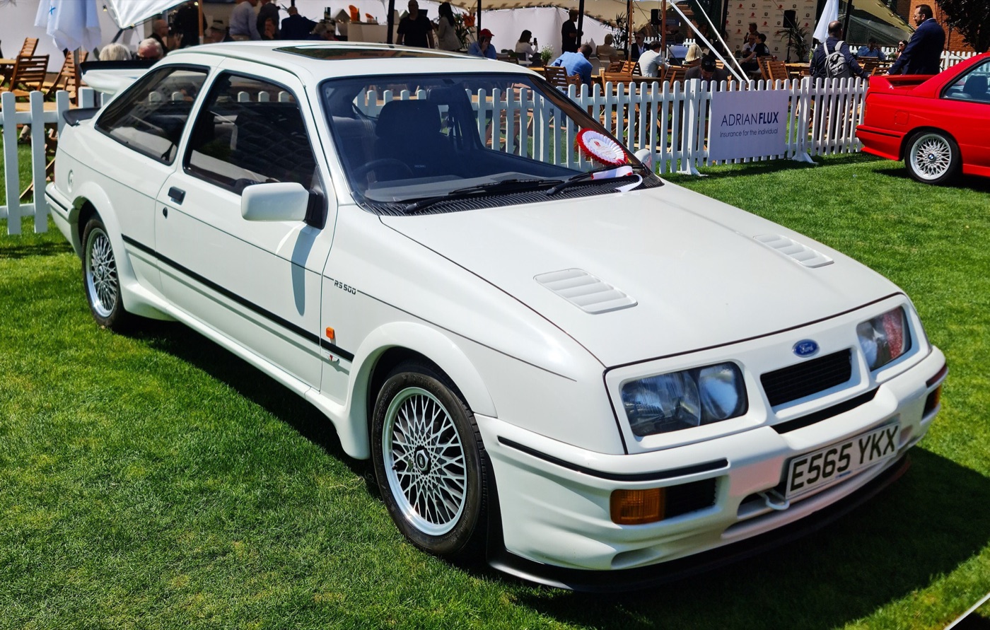 White Ford Sierra RS500 Cosworth with RS500 lettering on the front wing, a vented front bumper and spoked alloy wheels, parked on grass at a car show