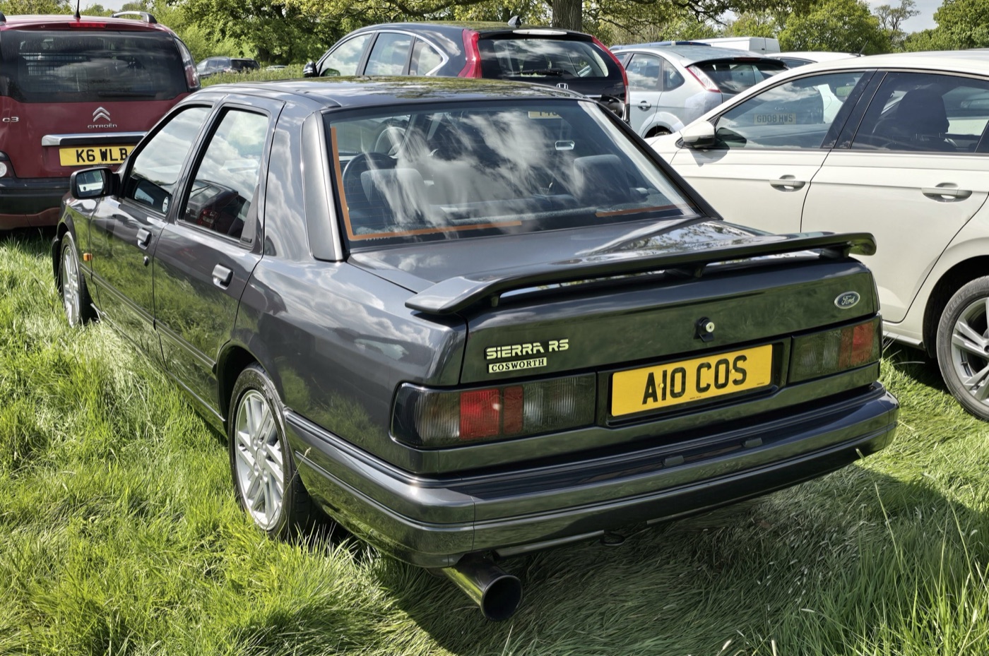 Dark grey four-door Ford Sierra Sapphire RS Cosworth seen from the rear, with a small boot spoiler and Sierra RS Cosworth badge, parked on grass