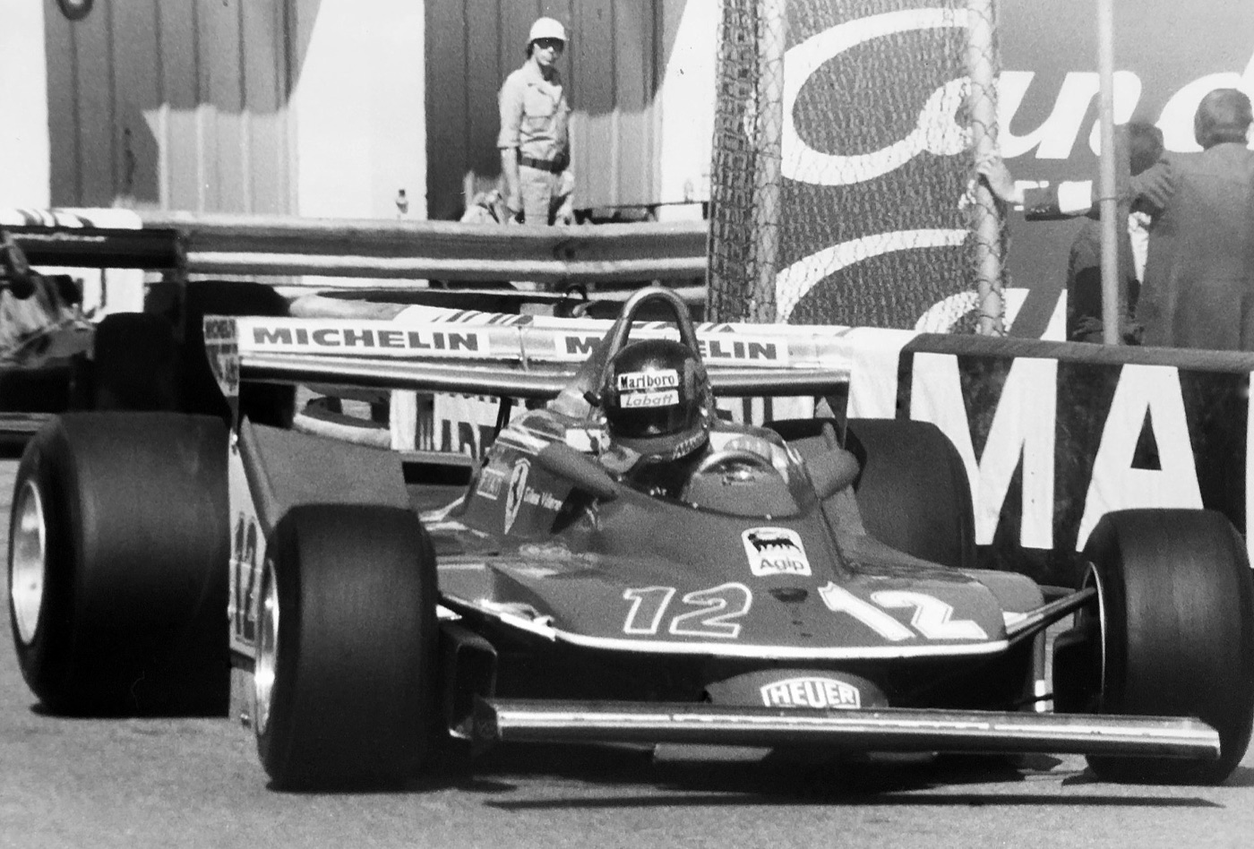 Black and white photograph of Gilles Villeneuve’s Ferrari 312 T4, number 12, turning through Rascasse at Monaco beside the barriers