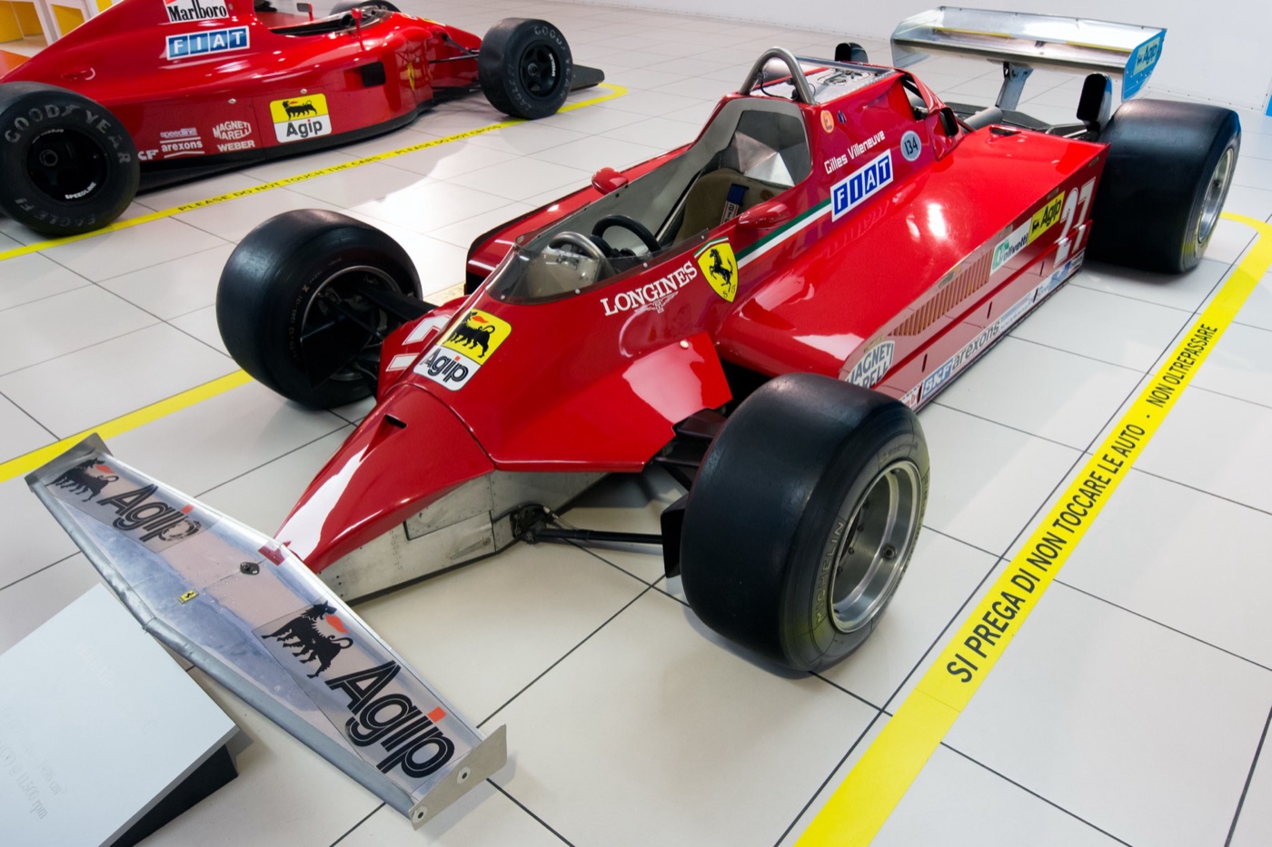 Red Ferrari 126 CK Formula One car, number 27, with Gilles Villeneuve’s name by the cockpit, displayed on a white tiled floor