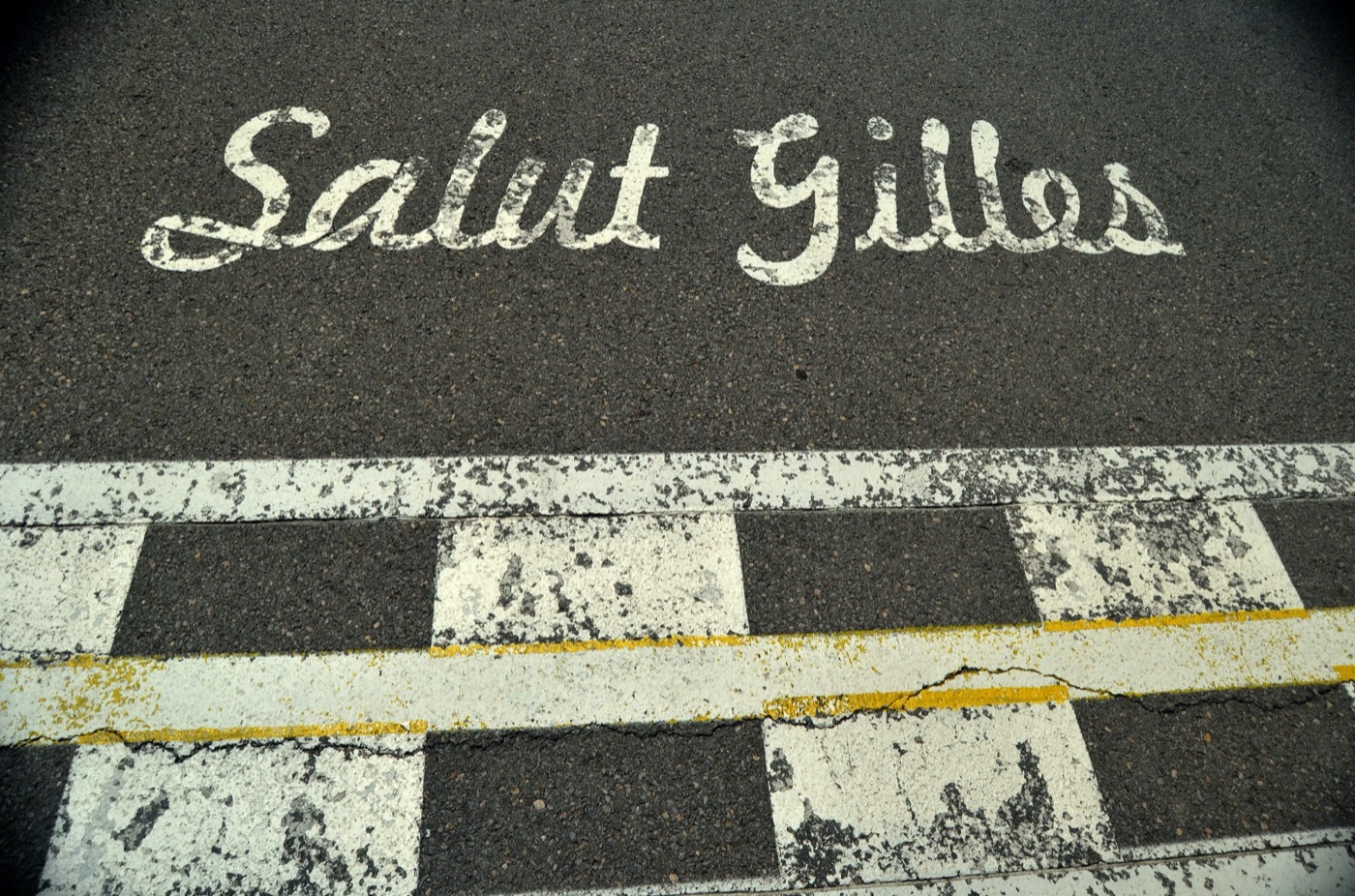 The words Salut Gilles painted in white script on the track beside a chequered start and finish line