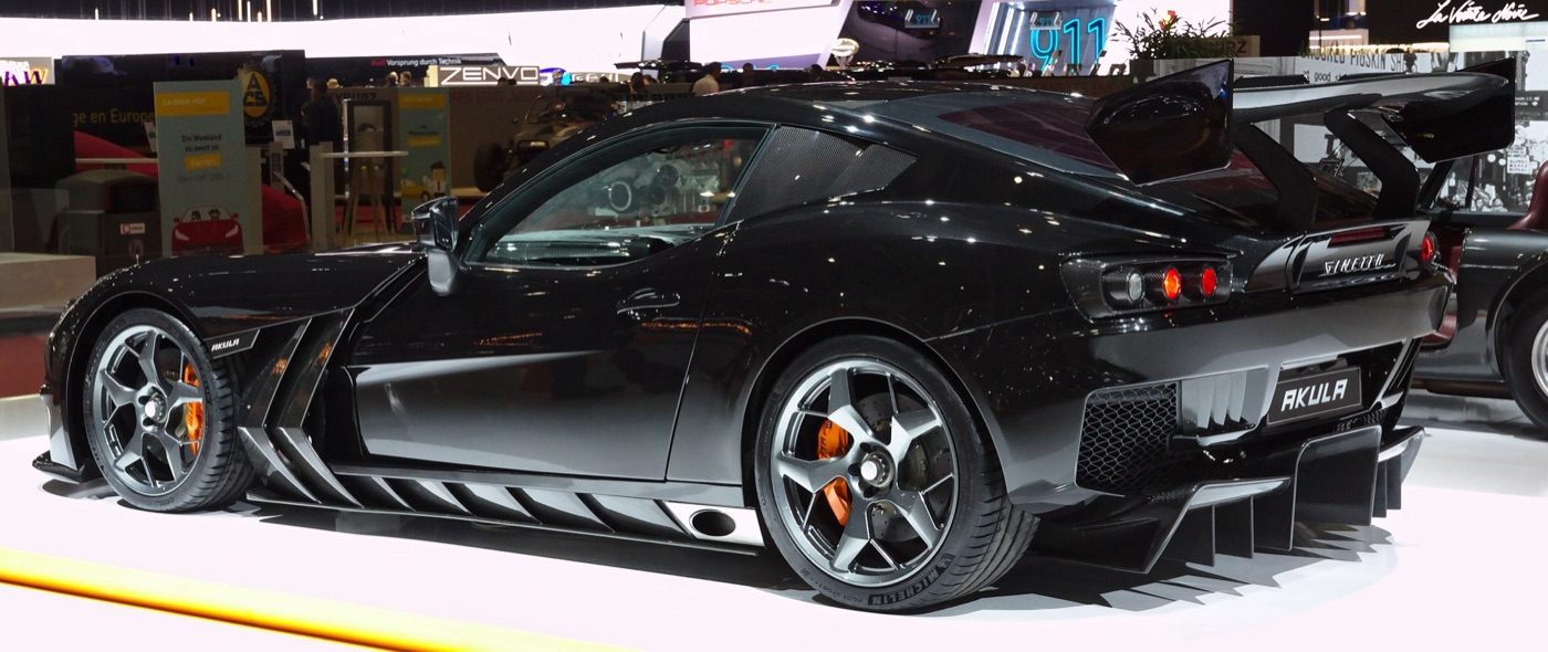 Black Ginetta Akula coupé with a large rear wing and orange brake calipers, seen from the side at a motor show