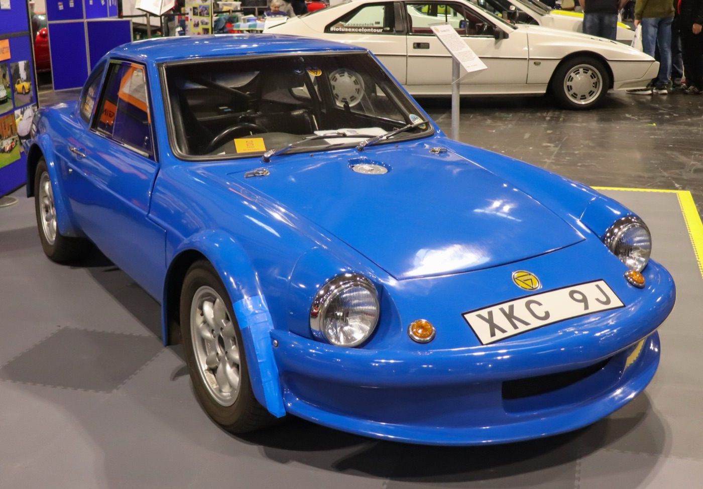 Blue 1970 Ginetta G15 coupé with chrome-rimmed headlamps on a show stand