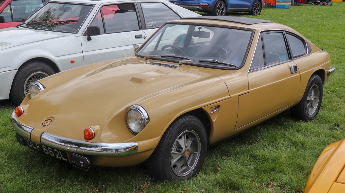 Gold 1971 Ginetta G21 fastback coupé with chrome bumpers, parked on grass