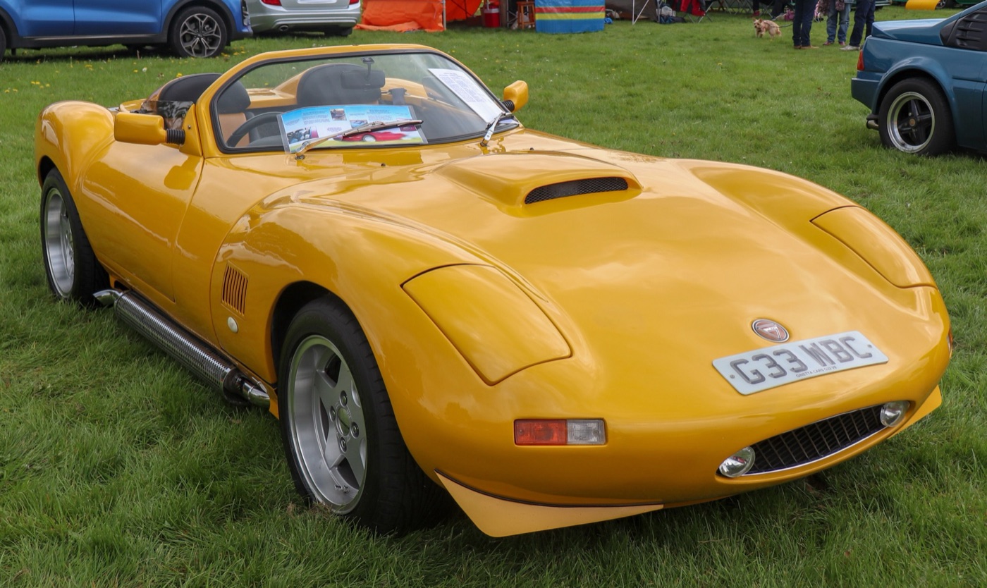 Yellow 1992 Ginetta G33 roadster with a bonnet scoop and side exhaust, parked on grass