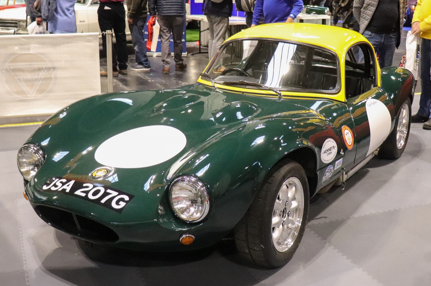 Dark green 1968 Ginetta G4 coupé with a yellow roof and white racing roundels on a show stand