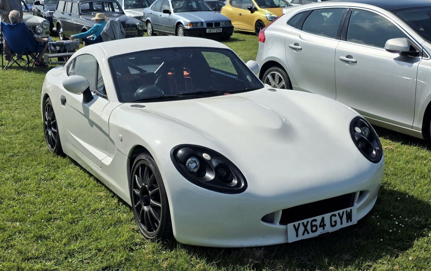 White 2014 Ginetta G40 coupé with black alloy wheels parked on grass at a car show