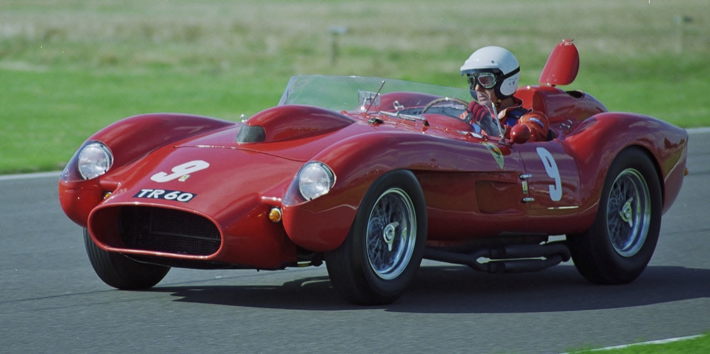 Red Ferrari 250 Testa Rossa sports racer, number 9, at speed on the Goodwood circuit with its driver in an open-face helmet and goggles