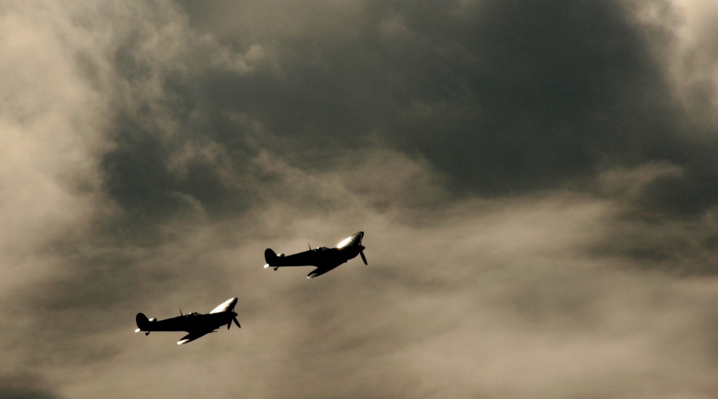 Two Supermarine Spitfires in silhouette against dark cloud over Goodwood