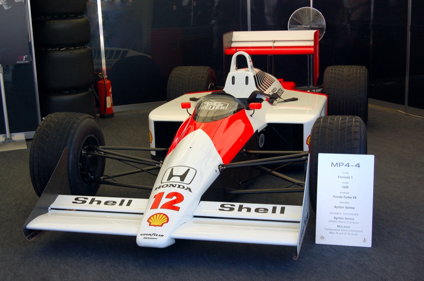 Red and white McLaren-Honda MP4/4 number 12 on display beside a sign listing its 1988 results