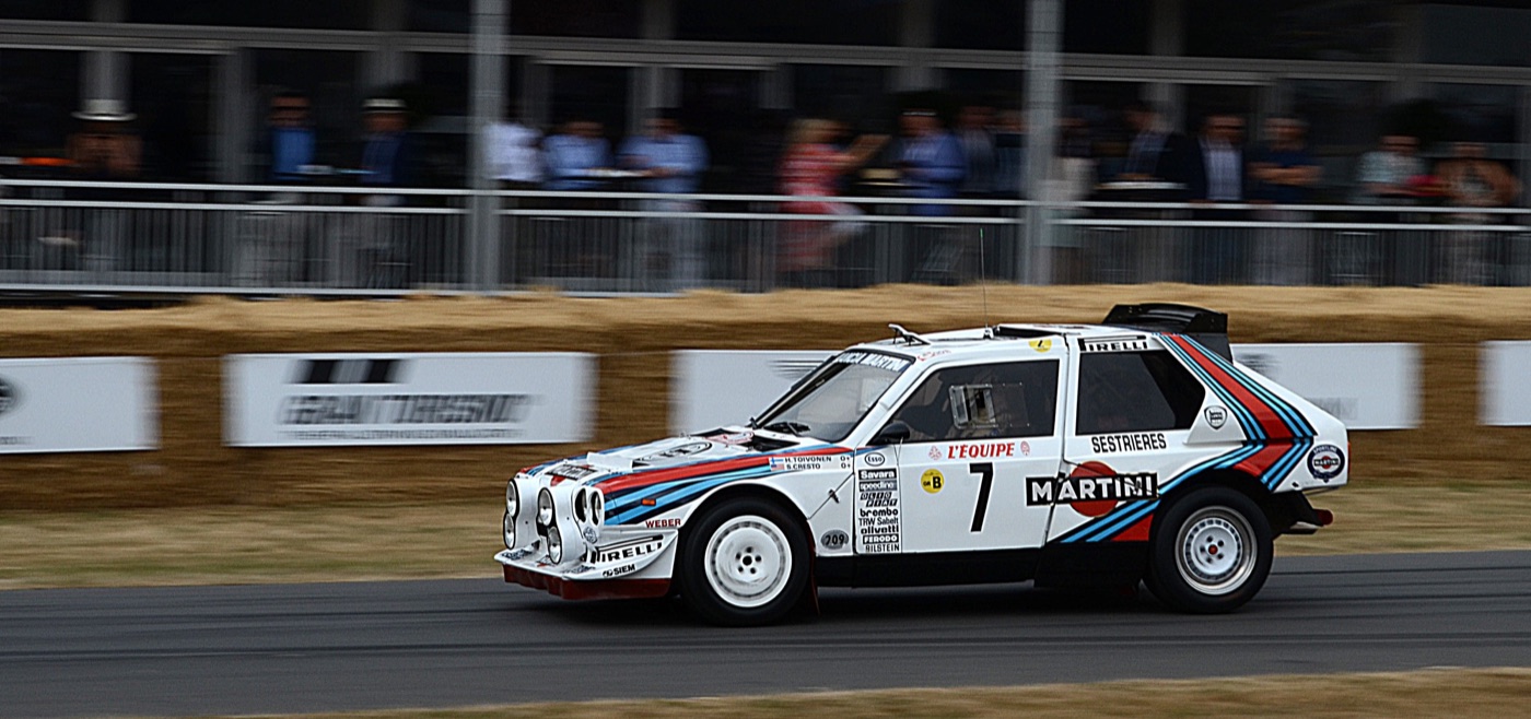 White Martini Lancia Delta S4, number 7, with the names H. Toivonen and S. Cresto on the wing, at speed past straw bales