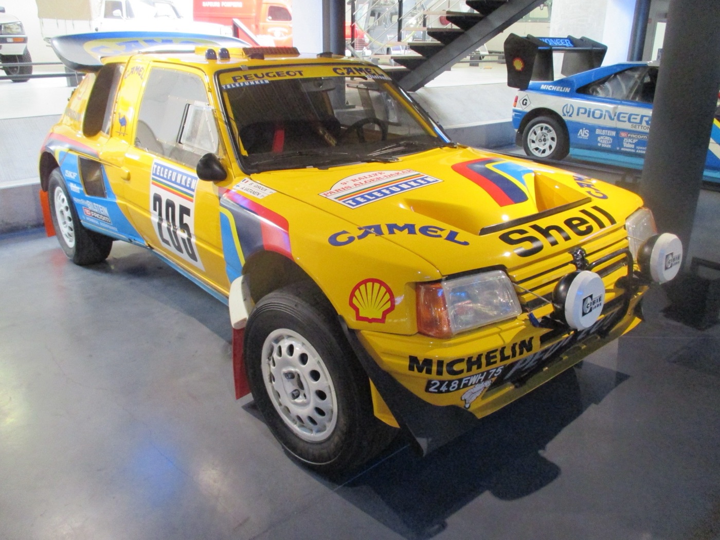 Yellow Peugeot 205 Turbo 16 Grand Raid, number 205, in Camel and Shell livery, on display indoors