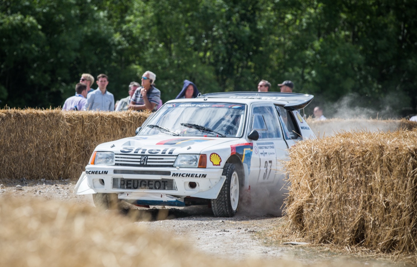 White Peugeot 205 Turbo 16 rally car in Shell and Michelin livery, number 37, sliding between straw bales on a gravel stage