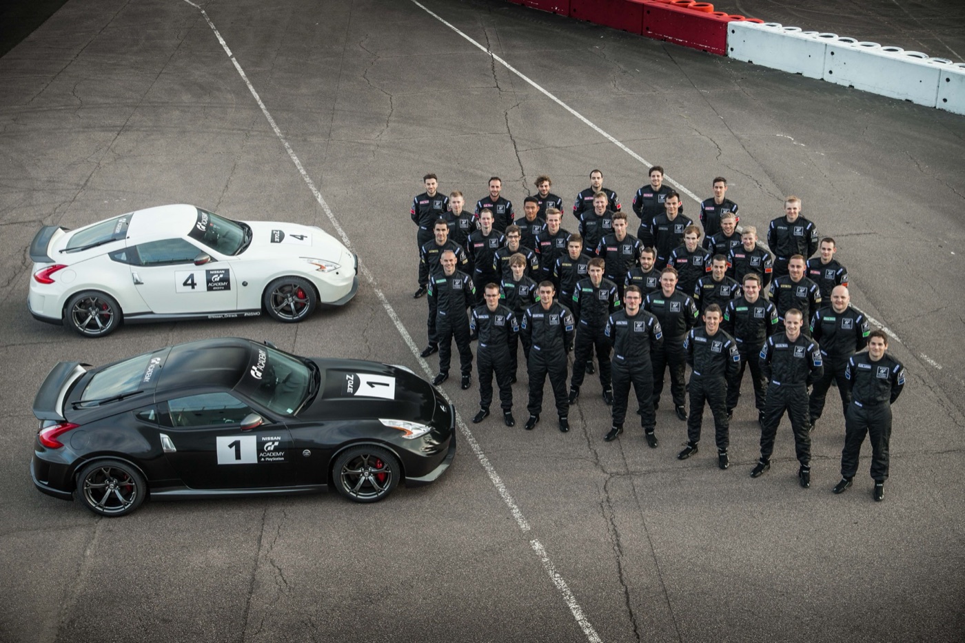 About forty finalists in black race suits lined up beside a white and a black Nissan 370Z Nismo in GT Academy livery