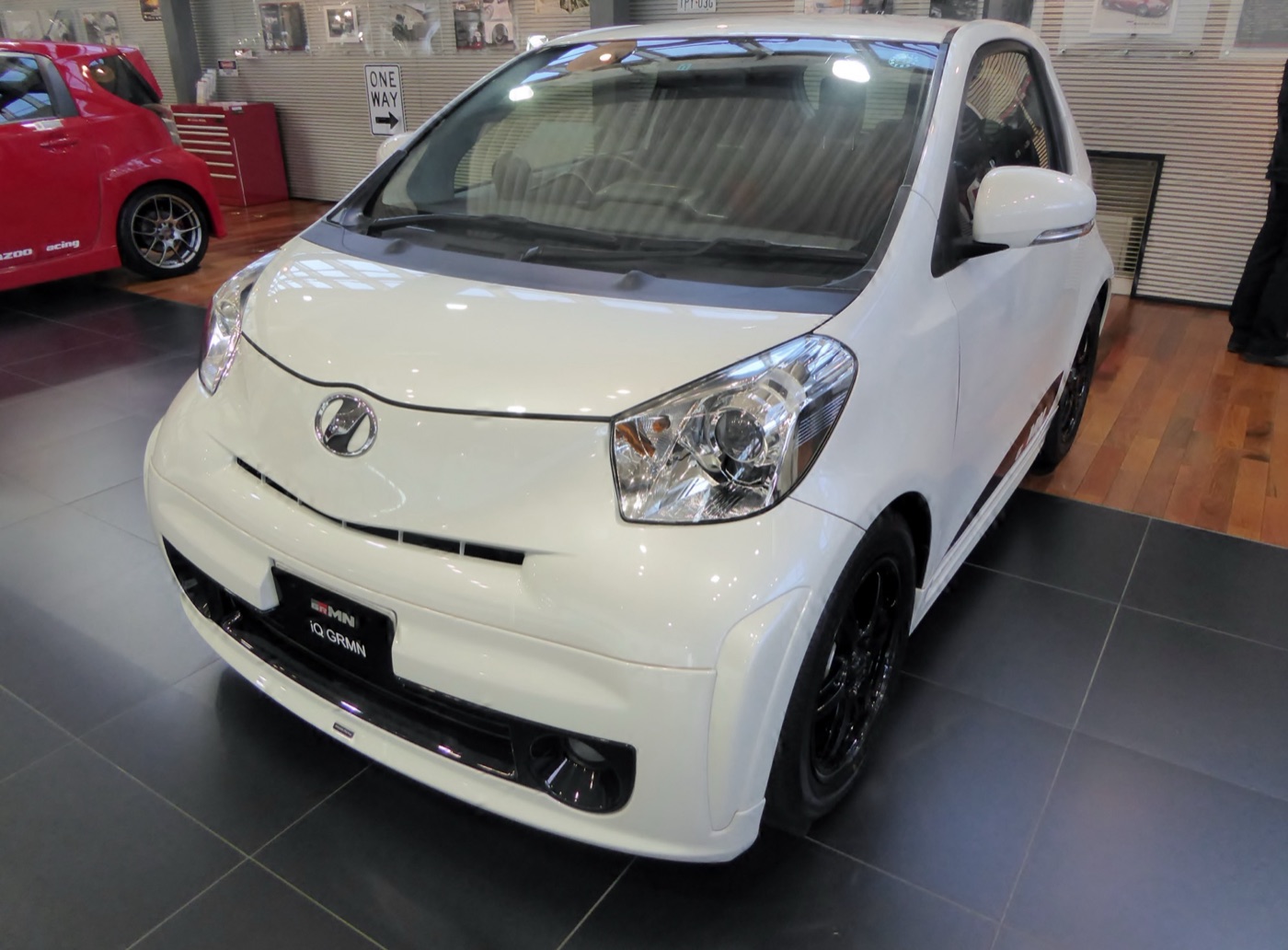 White Toyota iQ GRMN city car with black wheels and a GRMN badge on its front plate, in a showroom