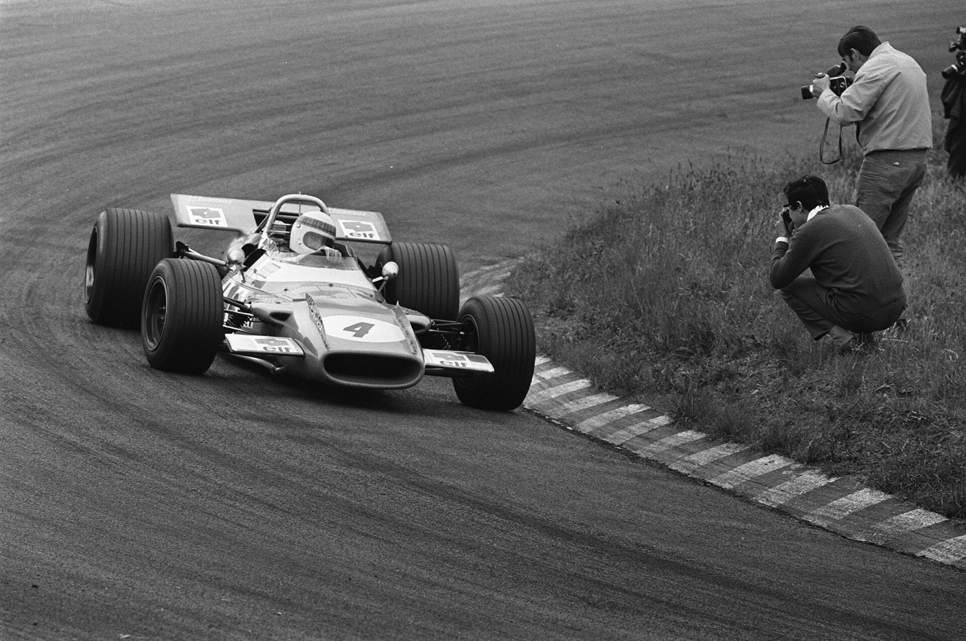 Black and white photograph of Jackie Stewart’s Matra MS80, number 4, rounding a kerbed corner at Zandvoort with photographers kneeling on the grass