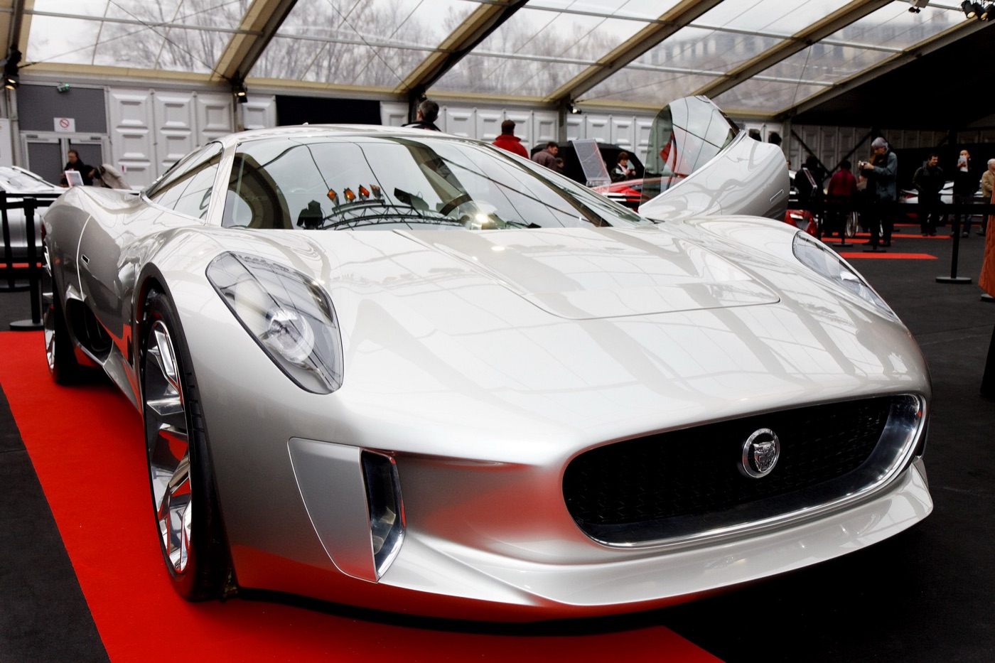 Front of the silver C-X75 concept with its oval grille and a swan-wing door open, in a glass-roofed exhibition tent