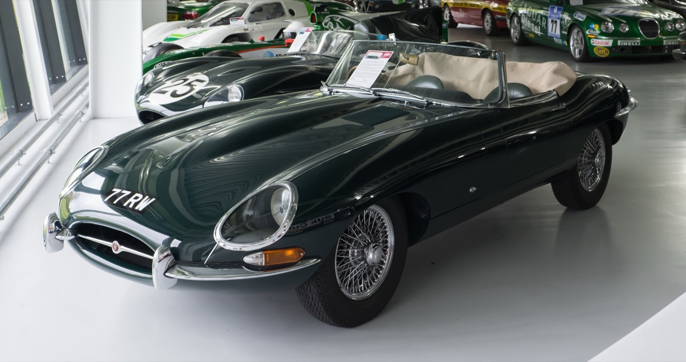 Dark green 1961 Jaguar E-Type roadster with the registration 77 RW, covered headlamps and wire wheels, indoors at a museum