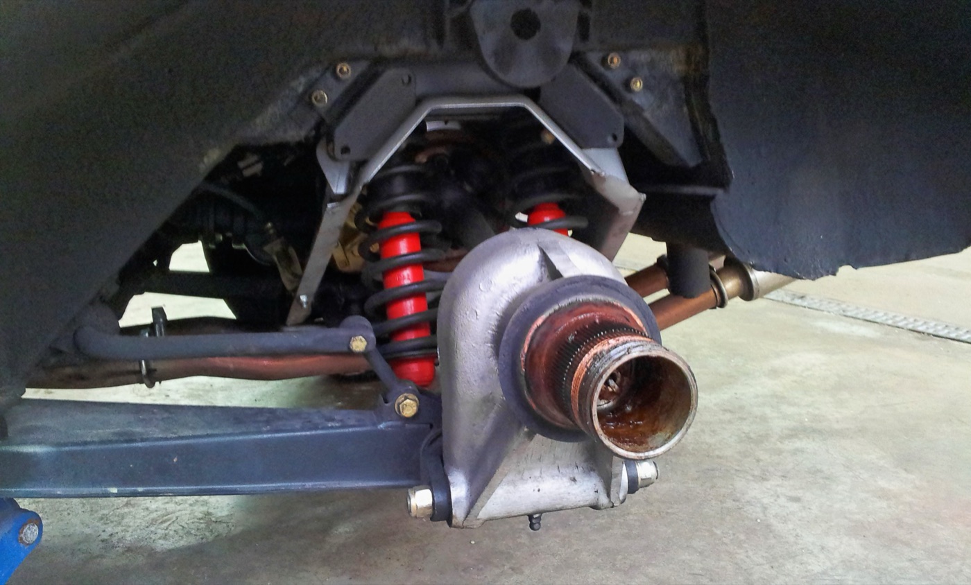 Underside view of an E-Type 4.2 rear suspension with twin red coil-spring dampers, trailing arm and hub carrier