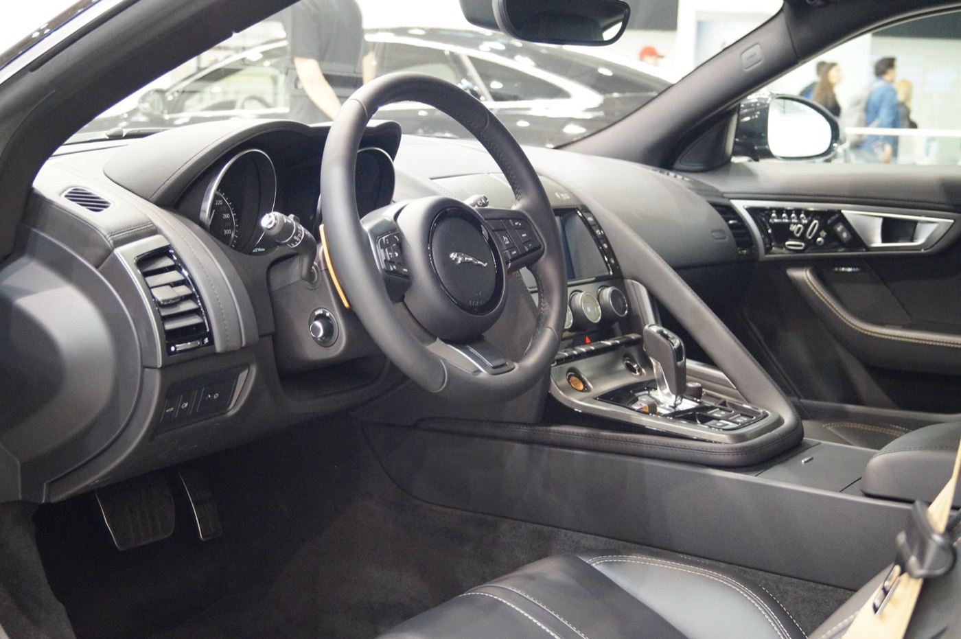 Black leather interior of a Jaguar F-Type coupe with the steering wheel, analogue dials and the grab handle along the passenger side of the console