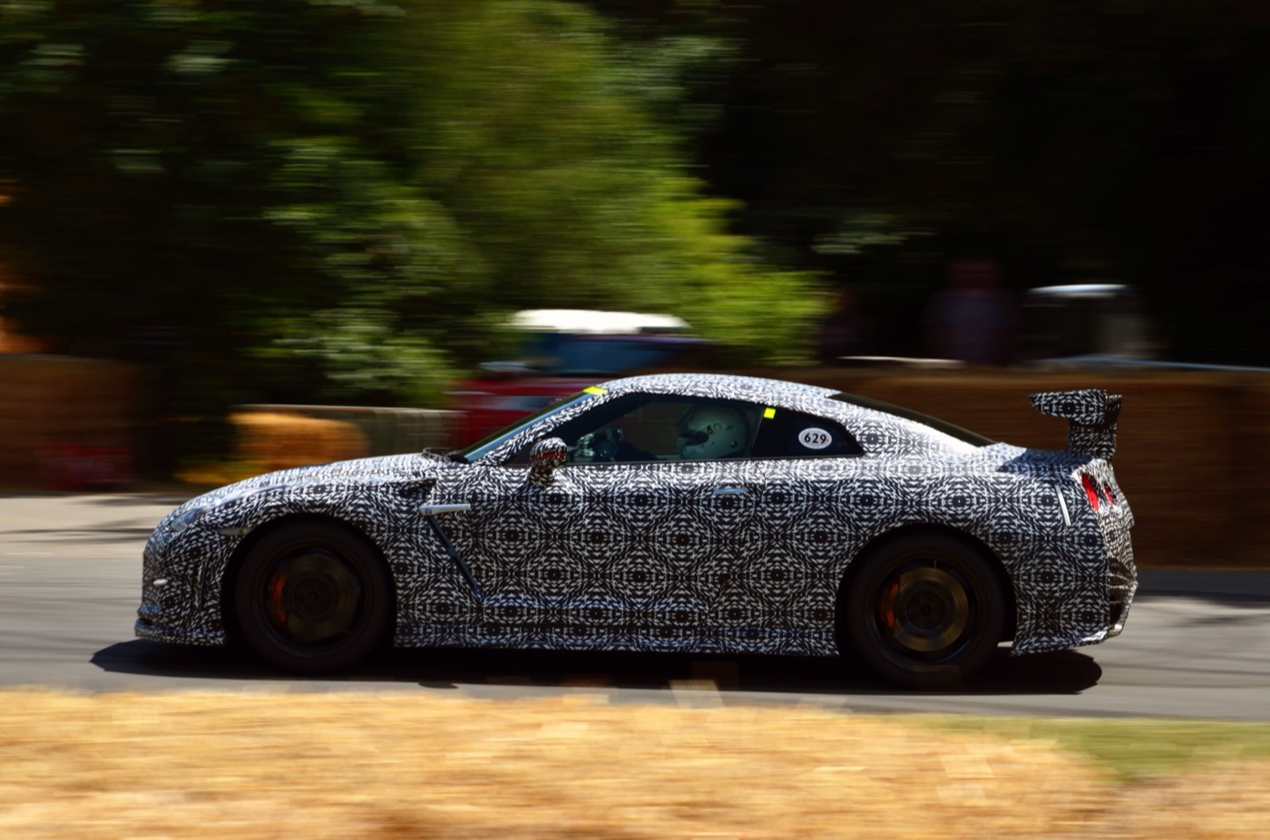 A Nissan GT-R in black and white camouflage wrap at speed on the Goodwood hill, trees blurred behind