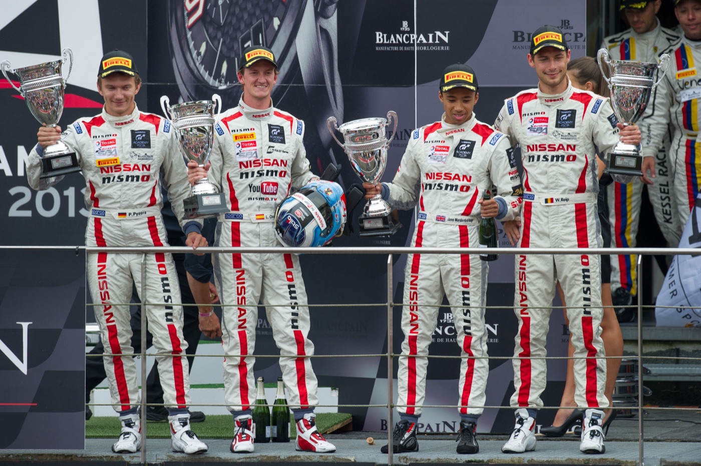 Four Nissan drivers in white race suits holding trophies on the Spa 24 Hours podium