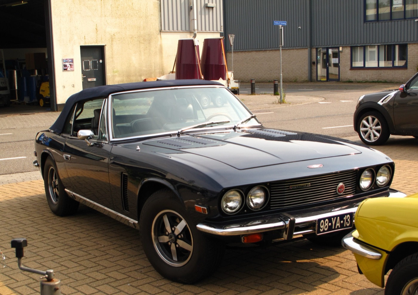 Dark blue 1975 Jensen Interceptor III Convertible with its black hood raised, parked on brick paving