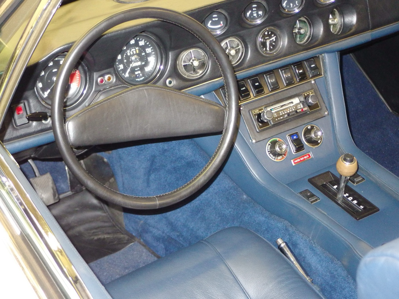 Dashboard of a Jensen Interceptor with round Smiths dials, a row of rocker switches above the radio and blue leather trim