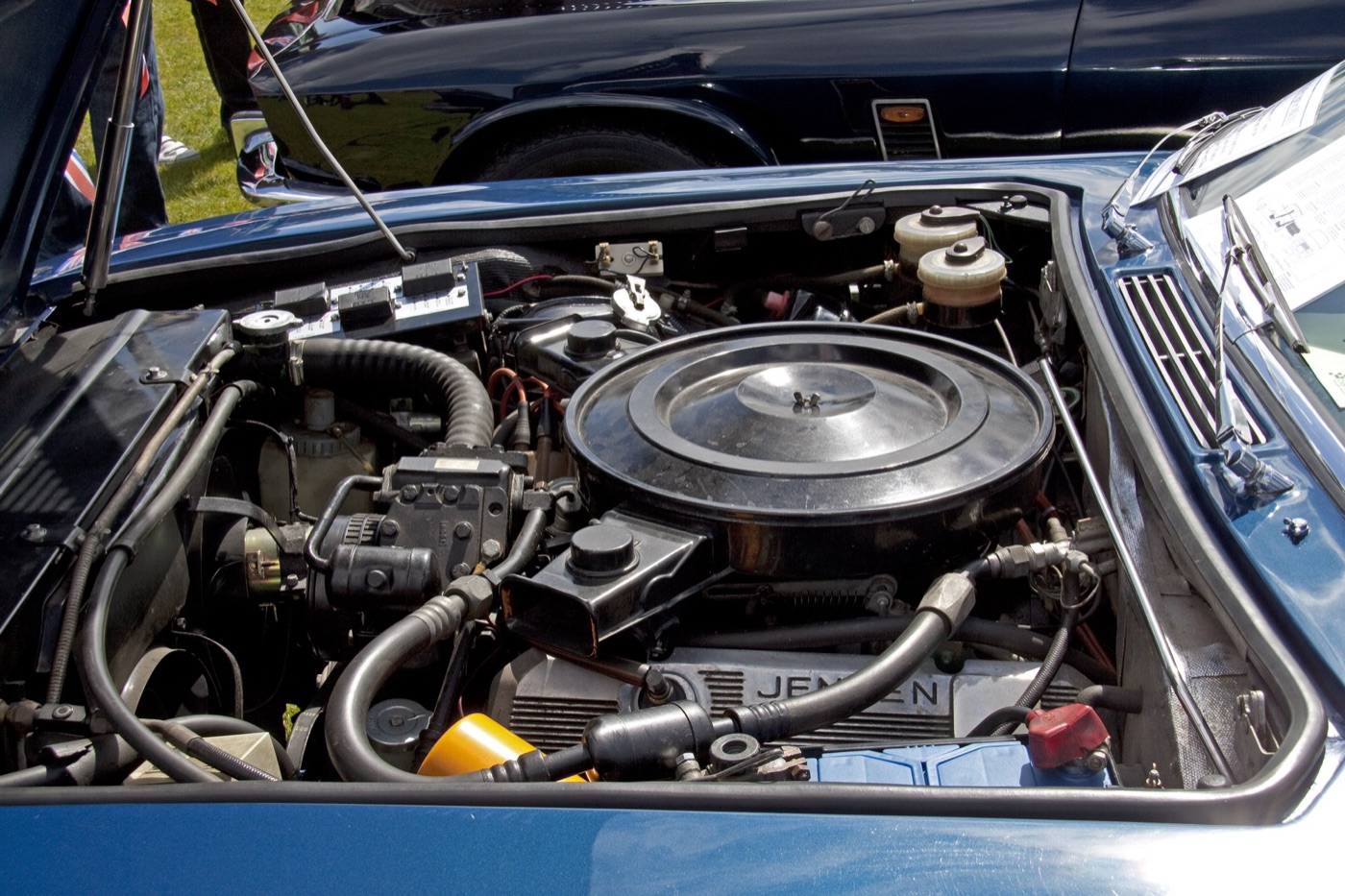 Engine bay of a blue Jensen Interceptor with the Chrysler V8, its round air filter and Jensen-script rocker cover