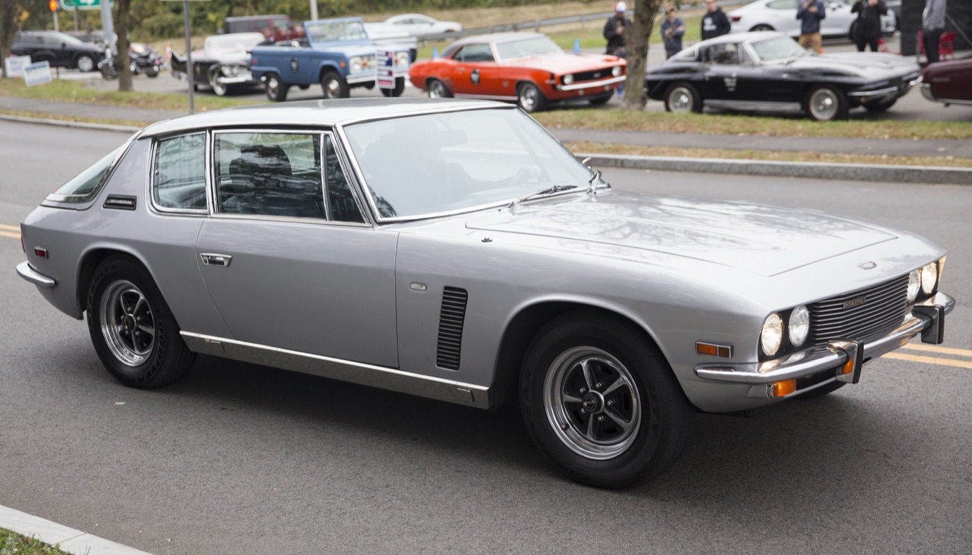 Silver 1971 Jensen Interceptor Mark II driving past parked classic cars