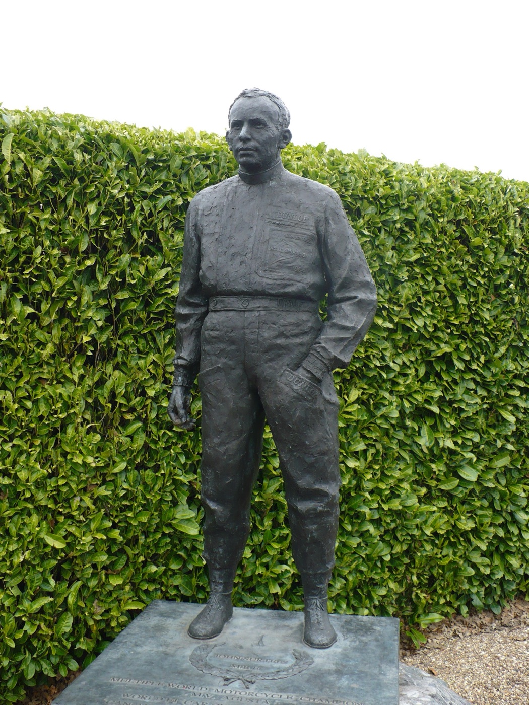 Bronze statue of John Surtees in racing leathers on a stone plinth in front of a laurel hedge