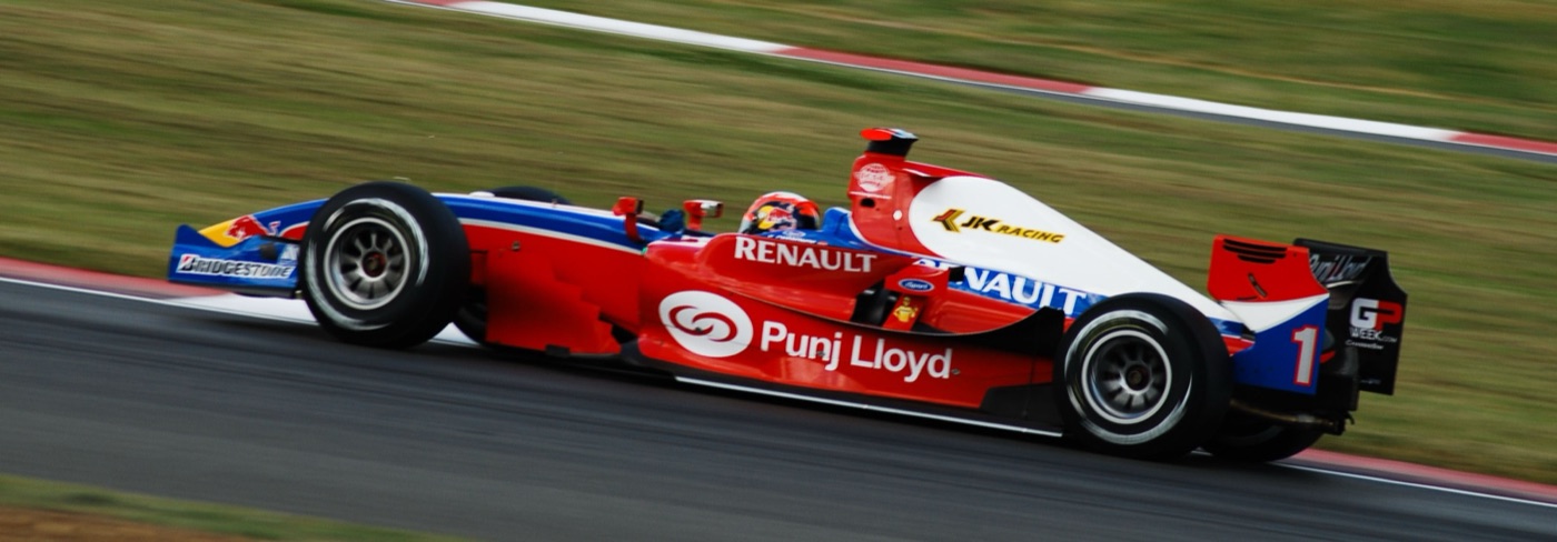 Red, white and blue iSport GP2 car with Punj Lloyd and Renault lettering, number 1, at speed on a grass-edged circuit