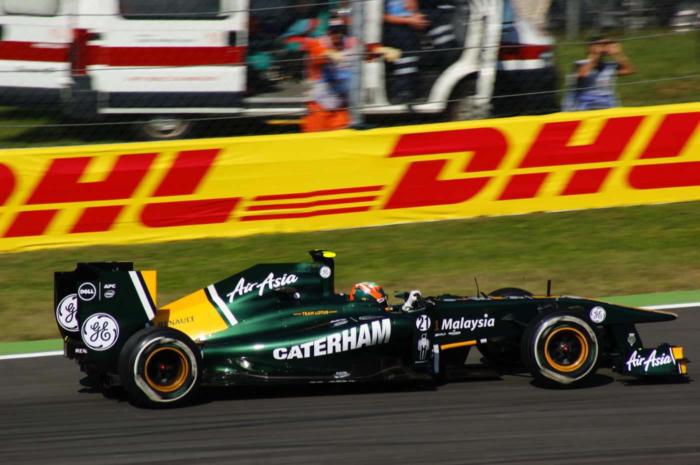 Dark green and yellow Team Lotus T128, number 21, with Caterham lettering on the sidepod, passing a red and yellow DHL advertising board at Monza