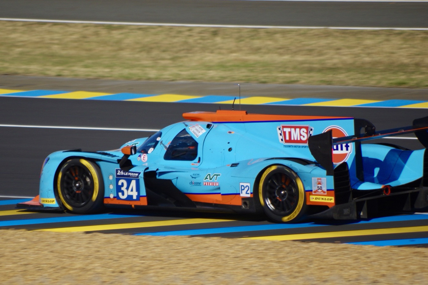 Light blue and orange Ligier LMP2 prototype, number 34, with TMS and P2 class stickers, on the kerbs at Le Mans