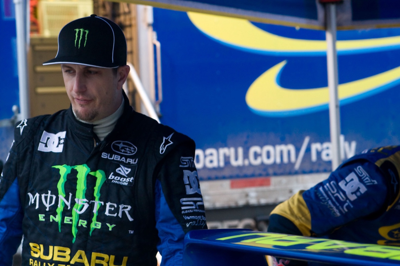 Ken Block in a Monster Energy and Subaru race suit beside the Subaru Rally Team USA truck