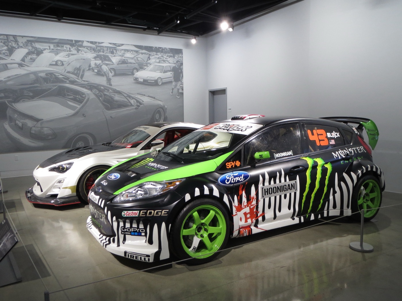 Black Ford Fiesta with green wheels, Monster Energy claws and Hoonigan stickers on display in a museum