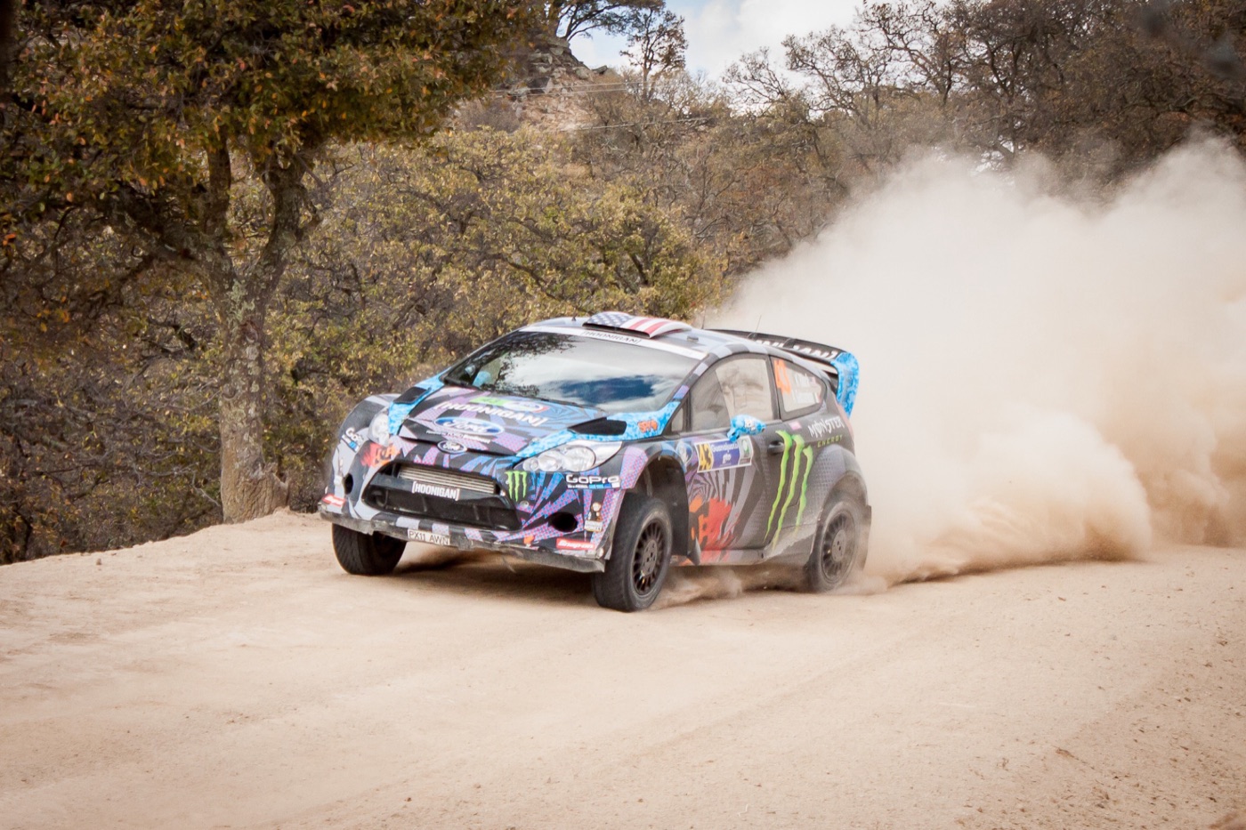 Ken Block’s Hoonigan Ford Fiesta RS WRC sliding on a dusty gravel stage, throwing up a cloud of dust