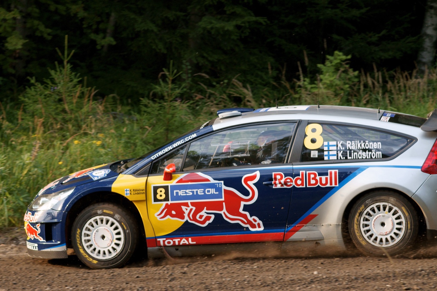 Blue and silver Citroën C4 rally car in Red Bull livery, number 8, on a gravel road beside a forest